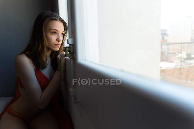 Девушка в нижнем белье смотрит в окно — стоковое фото