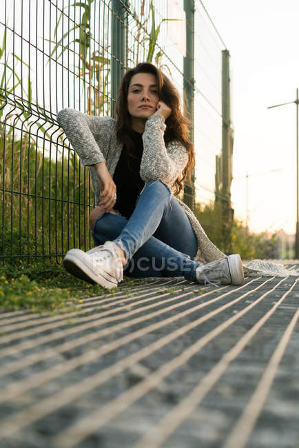 Woman posing on ground near fence — Stock Photo