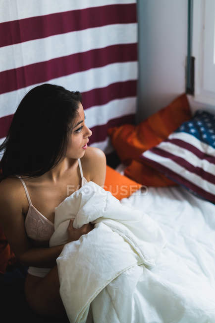 Femme assise sur le lit couvert de couverture — Photo de stock
