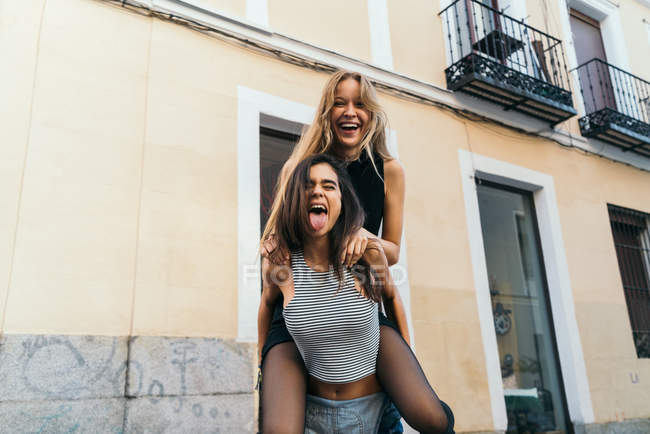 Cheerful friends piggy back riding in the street — Stock Photo