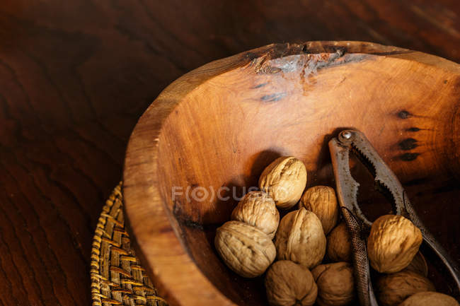 Crop wooden bowl with walnuts and tool for cleaning — Stock Photo