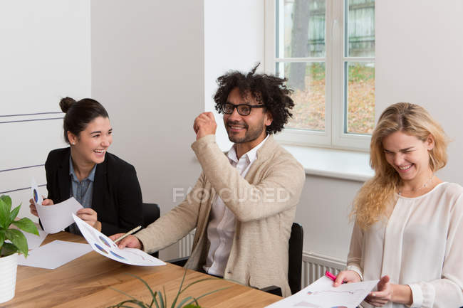 Три колеги сміються під час роботи над діаграмами в офісі — стокове фото