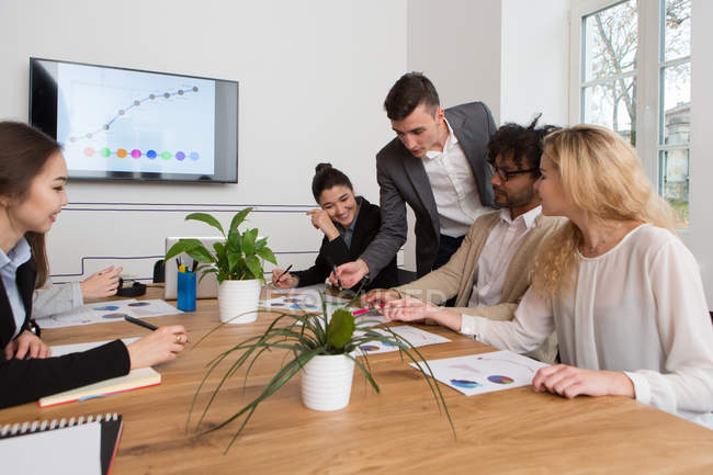 Group of co-workers sitting at desk and discussing diagrams together in light office. — Stock Photo