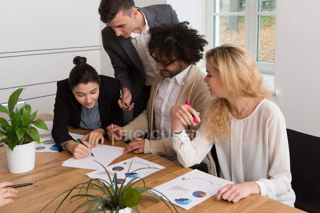 Co-workers sitting at desk and discussing diagrams together in light office. — Stock Photo