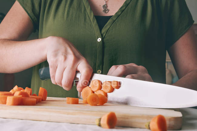 Gros plan de femme coupant carotte fraîche sur planche à découper en bois — Photo de stock