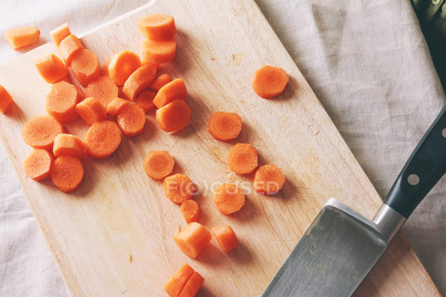 Chopped fresh carrot on wooden board with knife — Stock Photo