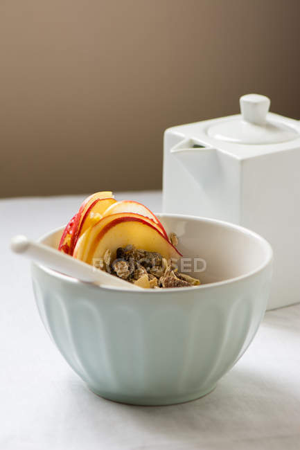 Cuenco blanco con granola y rodajas de fruta sobre mesa blanca - foto de stock