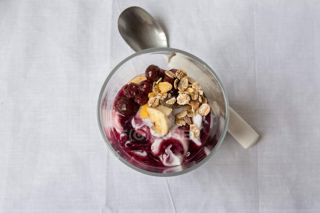 Glass of yoghurt with jam and granola with spoon on table — Stock Photo