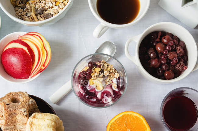 Top view of yoghurt with jam and granola, cups of cofee and fruits, concept of breakfast on table — Stock Photo
