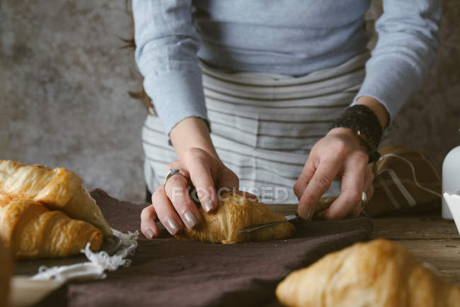 Руки женщины режут круассан — стоковое фото