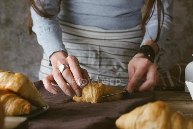 Manos femeninas rebanando croissant - foto de stock