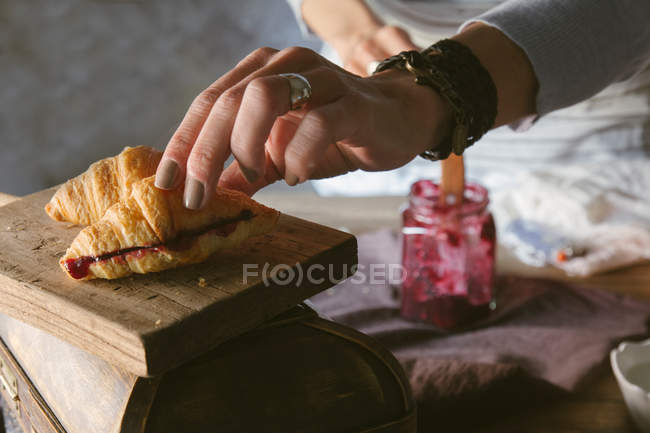 Mani femminili che chiudono croissant affettato con marmellata — Foto stock