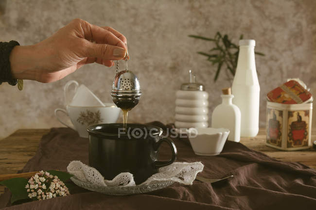 Mains tenant le tamis à thé sous la tasse — Photo de stock