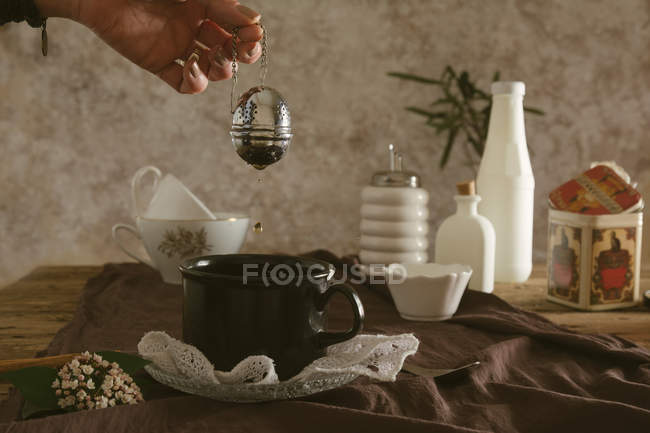 Mains tenant le tamis à thé sous la tasse — Photo de stock