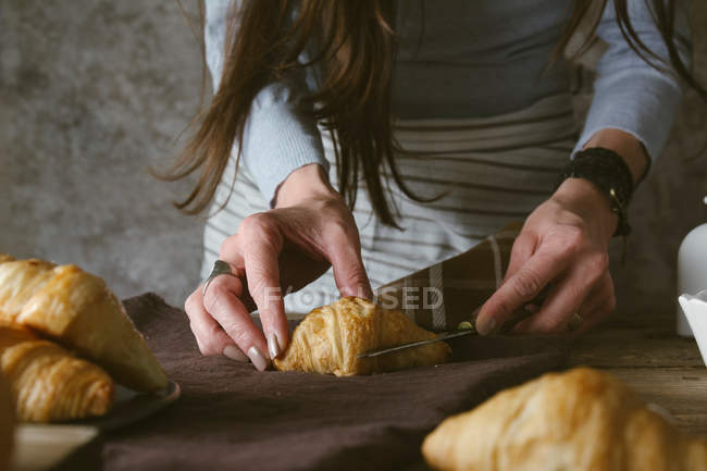 Mãos femininas cortando croissant — Fotografia de Stock