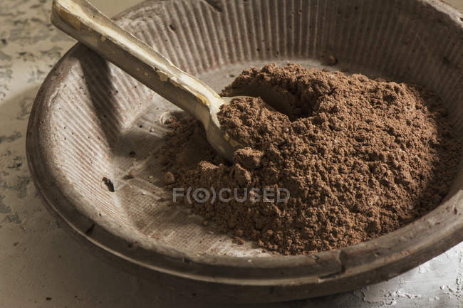 Still life of stone bowl with dark cocoa powder and wooden spoon — Stock Photo
