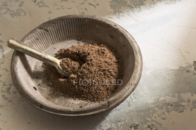 Stone bowl with dark cocoa powder and wooden spoon — Stock Photo