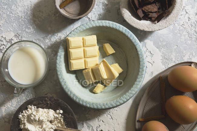 Tigela de cerâmica com barras de chocolate branco em meio a tigelas com vários ingredientes — Fotografia de Stock