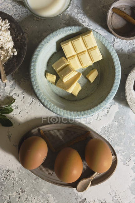 Directement au-dessus de la vue des bols avec des œufs et des barres de chocolat blanc — Photo de stock