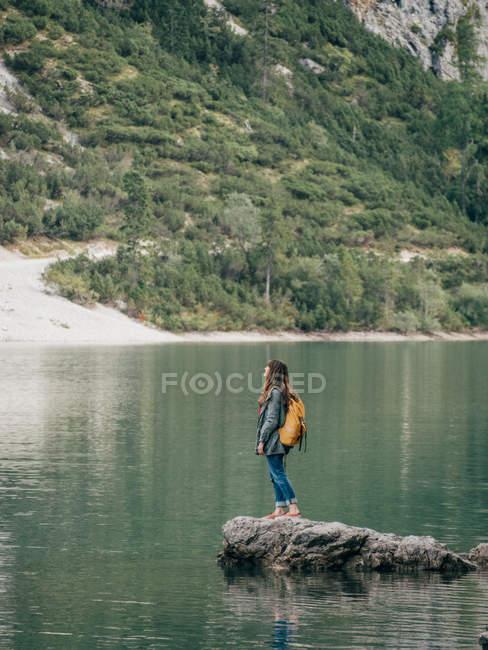 Female backpacker on stone in lake — Stock Photo