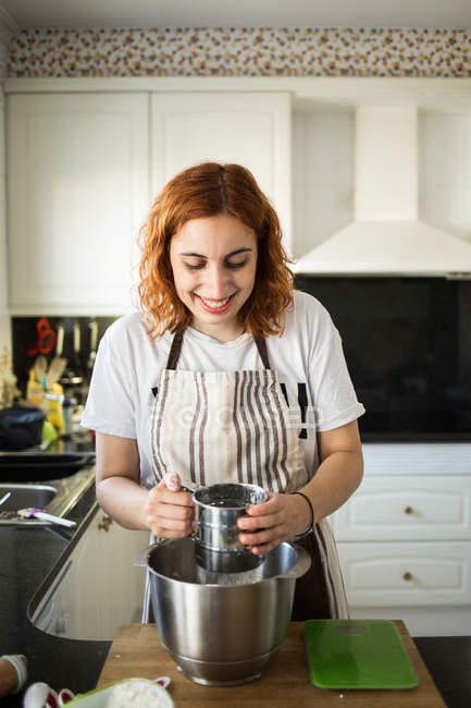 Cheerful woman adds flour — Stock Photo