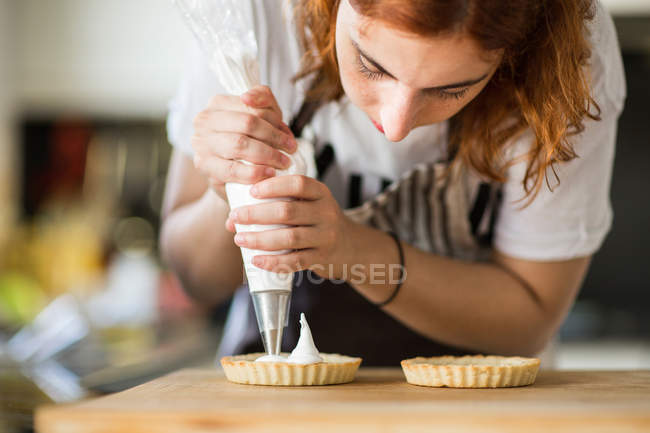 Woman putting cream on tarts — Stock Photo