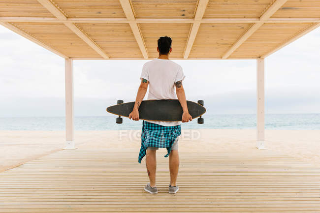 Человек со скейтбордом смотрит на море — стоковое фото