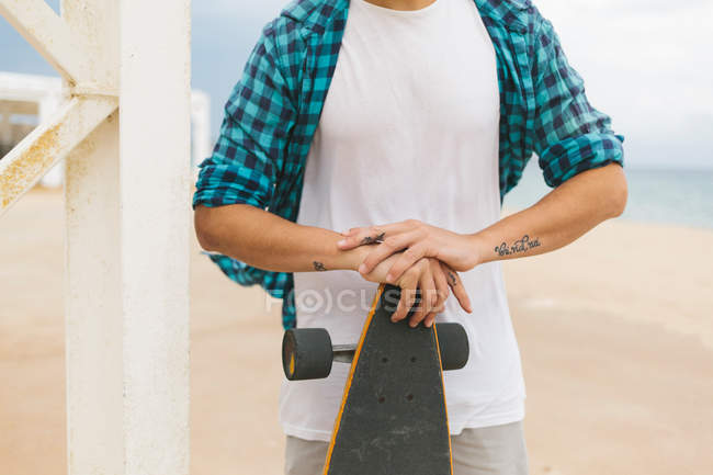 Homem segurando skate na praia de areia . — Fotografia de Stock