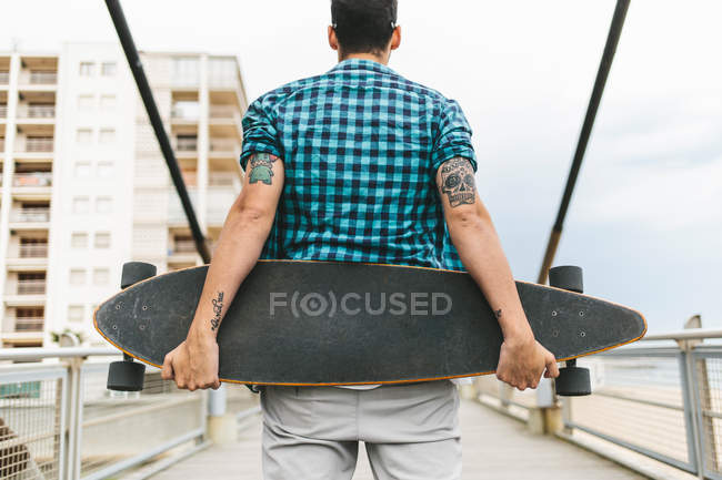 Чоловік з татуюваннями тримає скейтборд — стокове фото