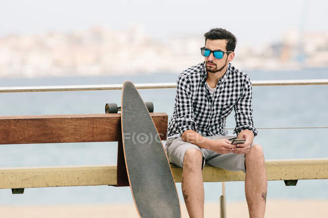 Junger Mann sitzt mit Smartphone auf Bank — Stockfoto