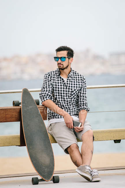 Young man sitting on bench with smartphone — Stock Photo