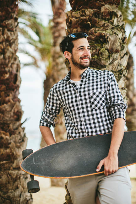 Mann mit Skateboard lehnt an Baum — Stockfoto