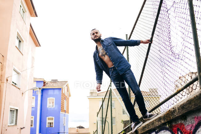 Человек в джинсах позирует на металлическом заборе — стоковое фото