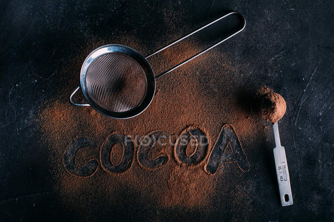 Powdered cocoa and strainer over dark — Stock Photo