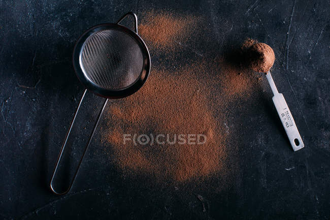 Powdered cocoa and strainer over dark — Stock Photo