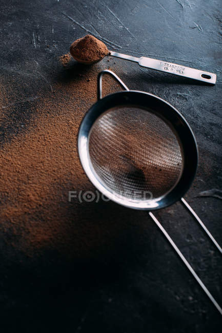 Cacao en polvo y colador sobre oscuro - foto de stock