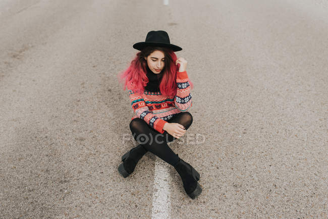 Mädchen mit Hut sitzt auf Fahrbahn — Stockfoto