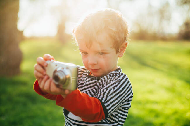 Niño en el campo tomando una foto con una cámara compacta - foto de stock