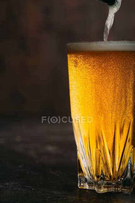 Verser de la bière dans un verre sur fond sombre — Photo de stock
