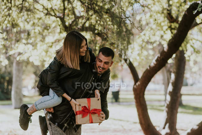 Cheerful man giving piggy back to girlfriend holding gift — Stock Photo