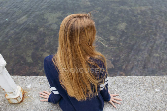 Girl sitting over on edge over sea — Stock Photo