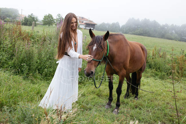 Girl in white dress stroking horse — Stock Photo