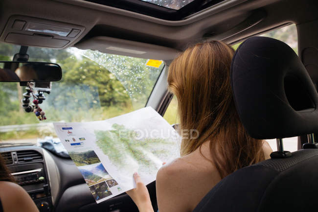 Girl sitting at passenger seat in car and reading map — Stock Photo
