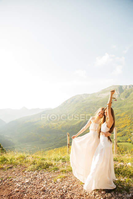 Retrato de dos chicas abrazadas vestidas de blanco y posando alegremente en el campo de montaña - foto de stock