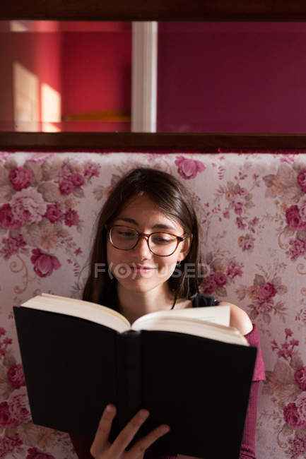 Mujer sonriente con libro en sofá - foto de stock