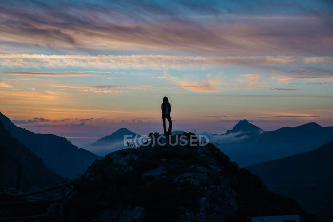 Silueta de chica de pie en la cima de la montaña sobre niebla puesta de sol cielo fondo - foto de stock