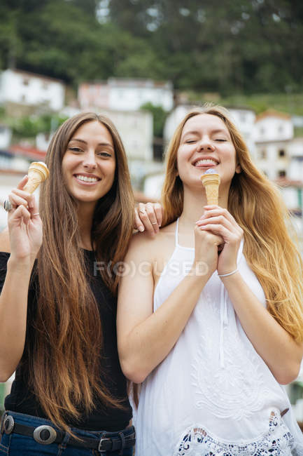 Портрет двух улыбающихся девушек с мороженым, позирующих над фасадами зданий — стоковое фото