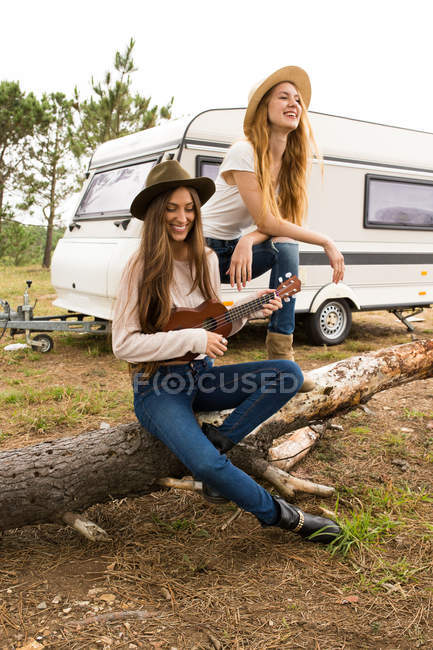 Two girls sitting on wood and playing ukulele — Stock Photo