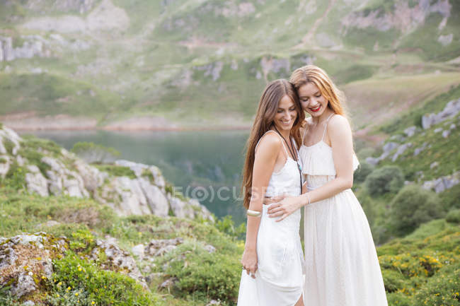 Portrait of smiling girlfriends hugging over mountain lake on background — Stock Photo