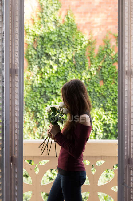 Chica joven oliendo rosas en la ventana - foto de stock